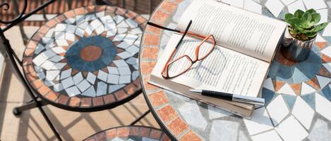 Une table ronde ornée d’un motif en mosaïque, un livre, une paire de lunettes et une petite plante en pot.