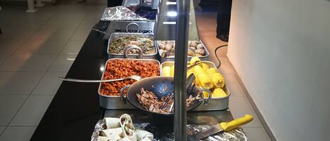 Una barra de buffet con diversos alimentos, incluyendo tortillas, maíz y ensaladas.