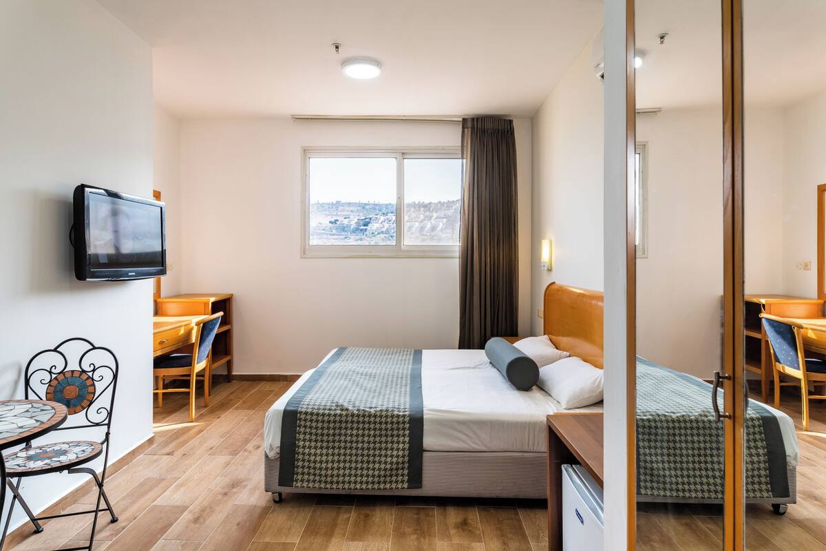 Une chambre d’hôtel équipée d’un lit, d’un bureau, d’une chaise, d’une télévision et d’une fenêtre donnant sur la ville.