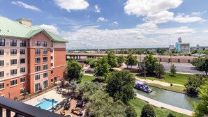 A hotel with a pool, outdoor seating, and a view of a river and distant buildings.