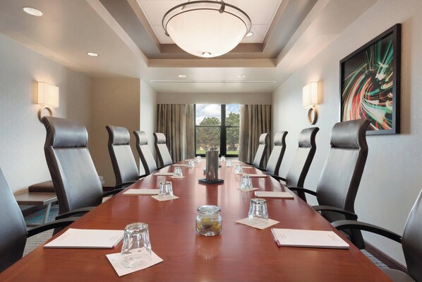 A conference room with a long table, chairs, a chandelier, and a painting on the wall.