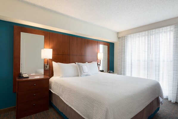 Habitación de hotel con una cama grande, cabecera de madera, mesita de noche con lámpara y una ventana con cortinas.