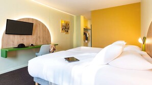 Habitación de hotel con cama, escritorio con silla, televisor de pantalla plana en la pared y espejo.