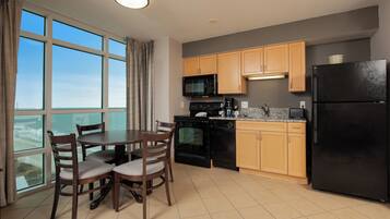 A modern kitchen with wooden cabinets, a black refrigerator, a microwave, and a coffee maker. There is a dining table with chairs and a large window offering a view.