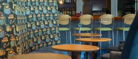 A bar area with multiple wooden tables and chairs, a patterned wall, and shelves with bottles.