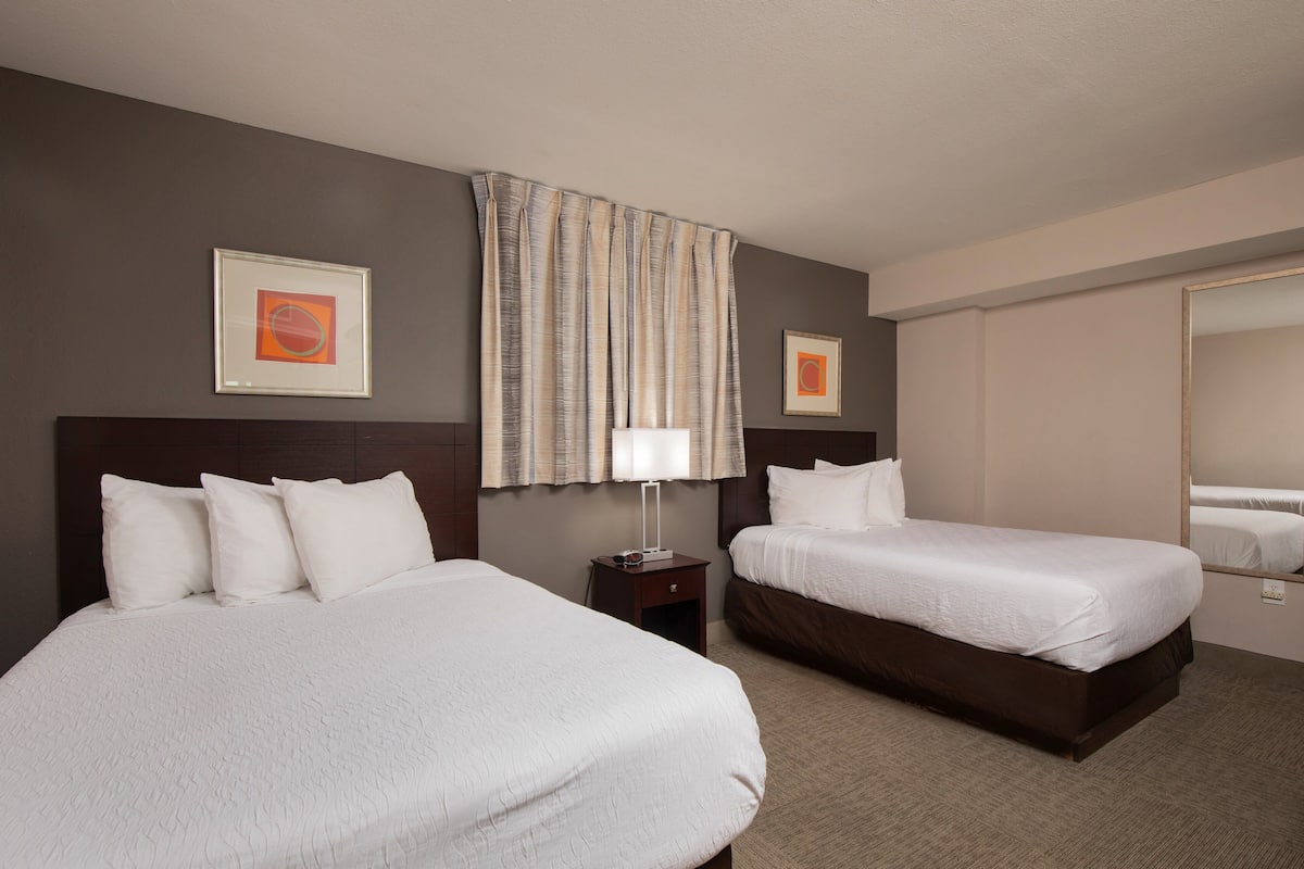A hotel room with two beds, a nightstand, a lamp, and two framed pictures on the wall.