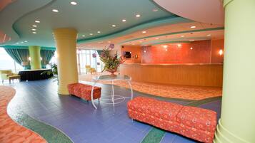 Un hall de hotel con mostrador de recepción, zona de estar y una planta grande.