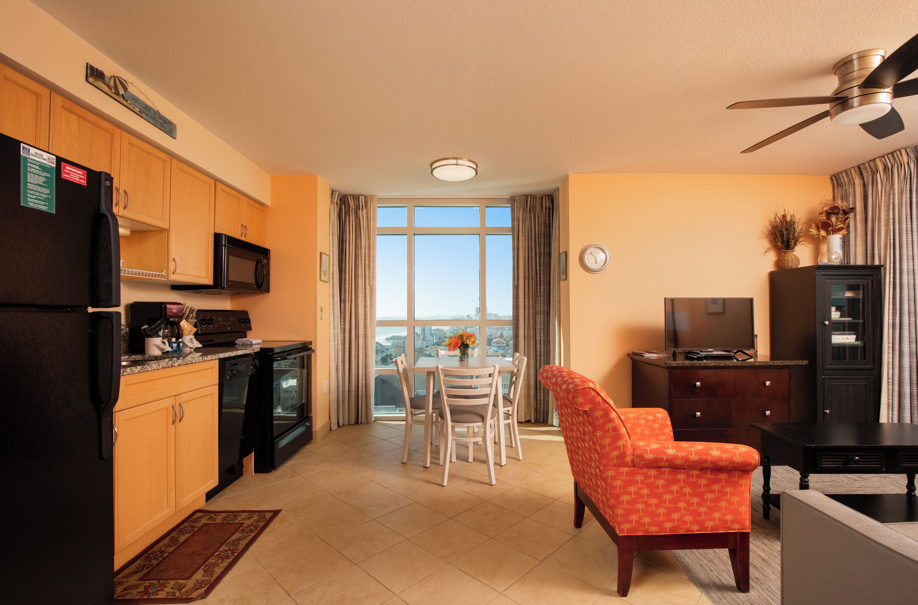 A compact kitchen with a refrigerator, microwave, and stove, a dining area with a table and chairs, and a seating area with a sofa and TV stand.