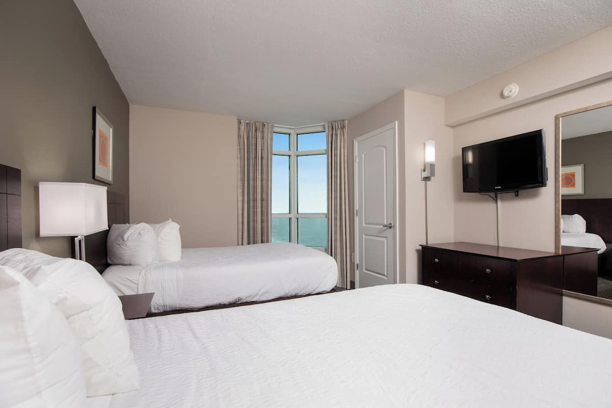 A hotel room with two beds, a TV, a dresser, and a window with curtains.