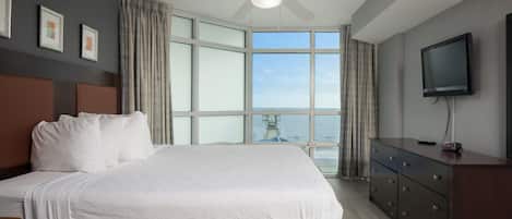 A hotel room with a large bed, a ceiling fan, a TV, and a view of the ocean.