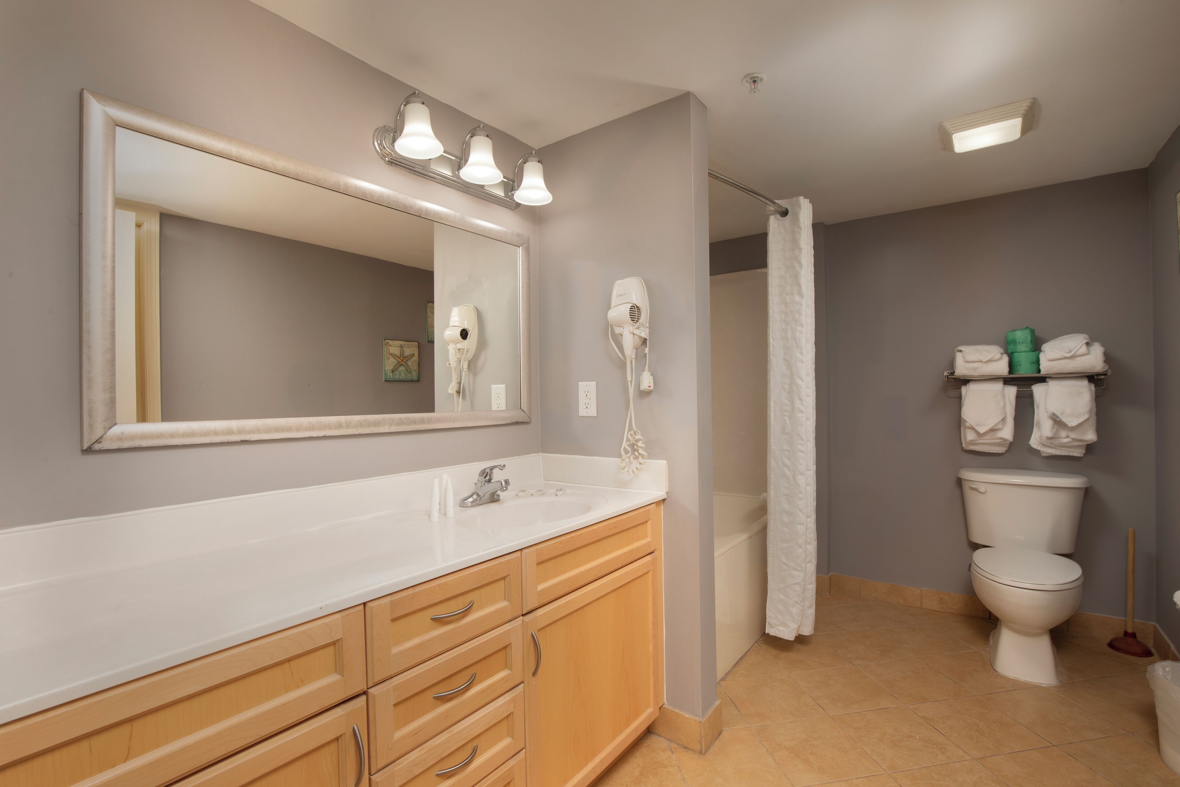 A bathroom with a large mirror, vanity with drawers, a toilet, and a shower curtain.