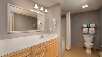 A bathroom with a large mirror, vanity with drawers, a toilet, and a shower curtain.