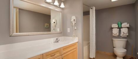 A bathroom with a large mirror, vanity with drawers, a toilet, and a shower curtain.