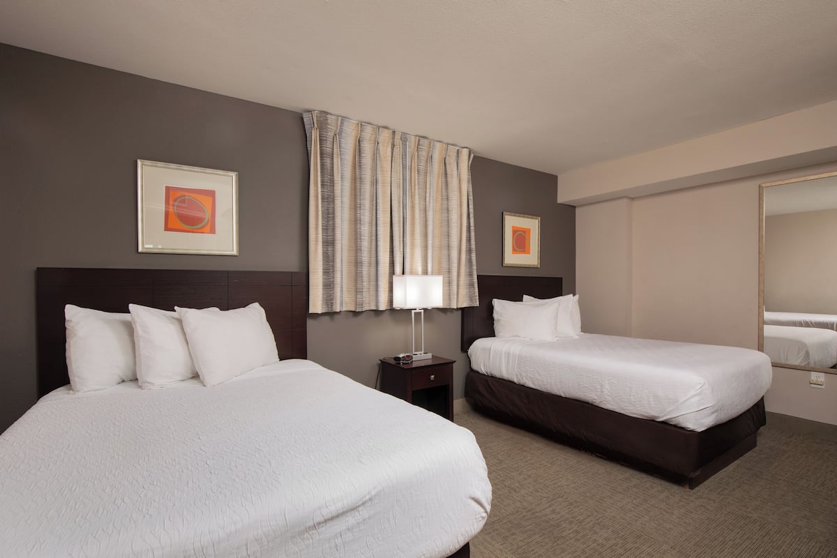 A hotel room with two beds, a nightstand, a lamp, and two framed artworks on the walls.