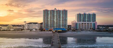 A waterfront hotel with a pier leading to the beach, featuring multiple high-rise buildings and a water tower.
