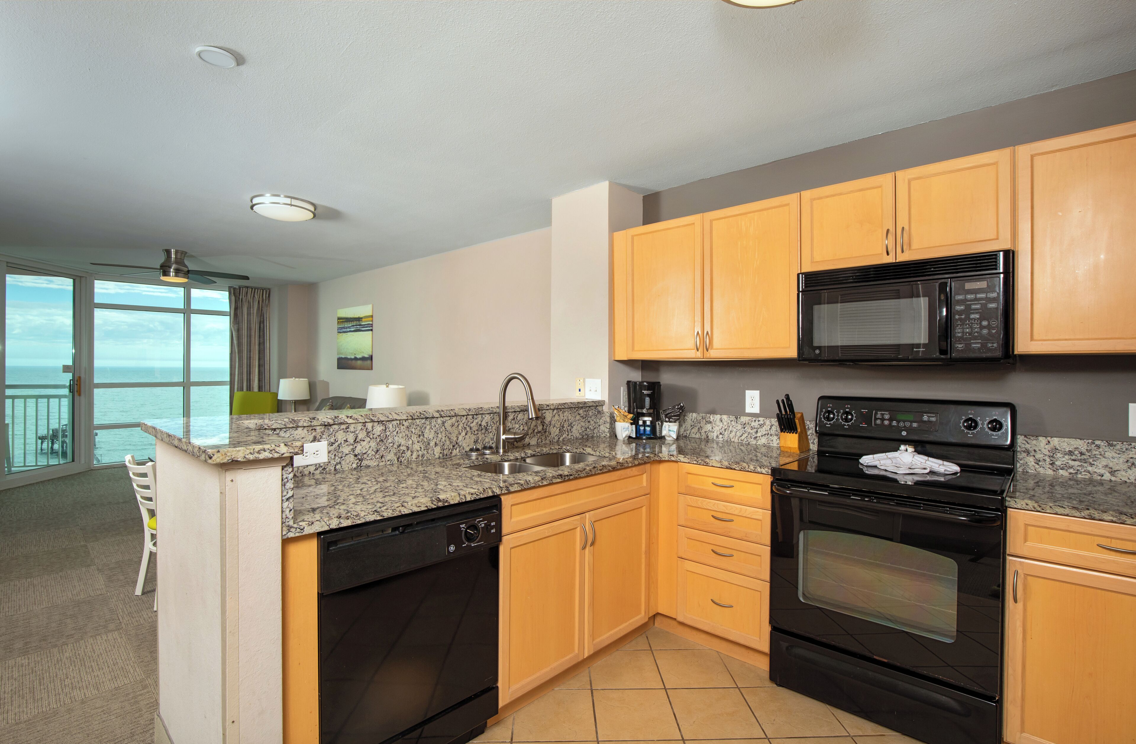 A modern kitchen with granite countertops, wooden cabinets, a black microwave, and a stove.