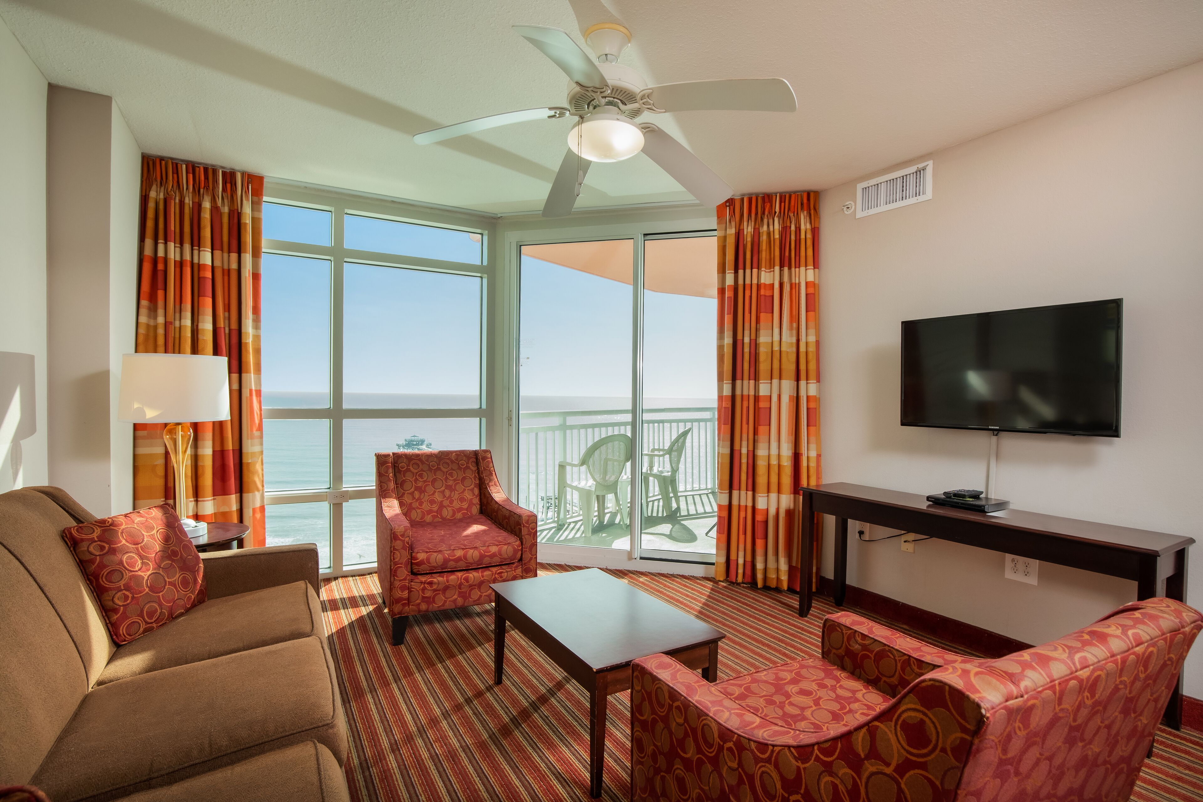 Una habitación de hotel con sofá, sillón y televisor sobre un mueble.