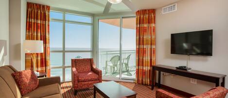 A hotel room with a sofa, armchair, and a TV on a stand.