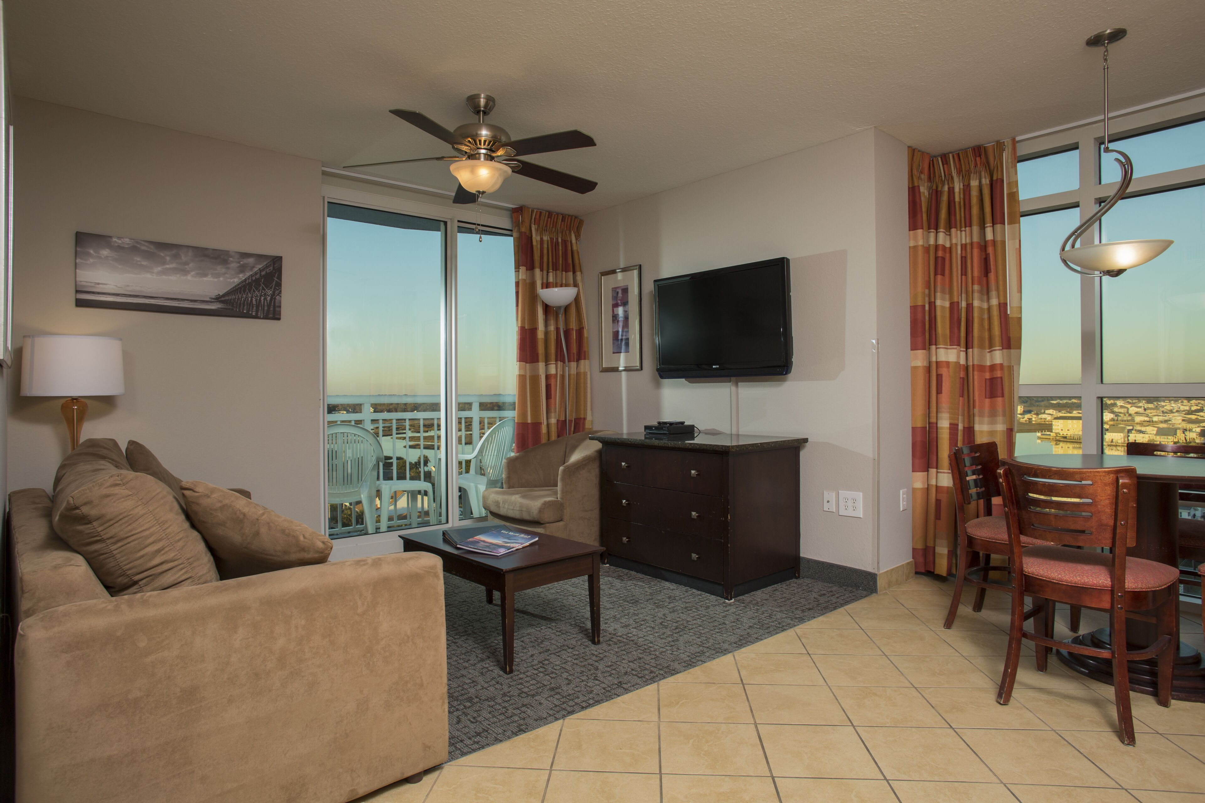 A hotel room with a sofa, coffee table, TV, and a balcony with a view.