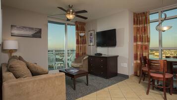 A hotel room with a sofa, coffee table, TV, and a balcony with a view.