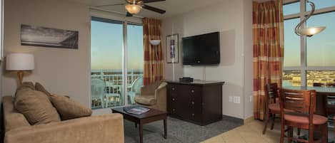 A hotel room with a sofa, coffee table, TV, and a balcony with a view.