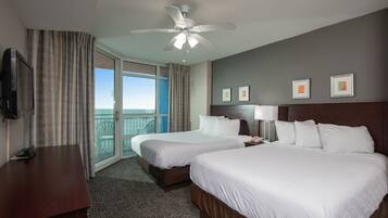A hotel room with two beds, a desk, a TV, a ceiling fan, and a balcony with a view.