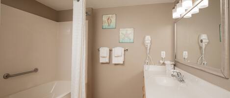 A bathroom with a bathtub, a sink, a mirror, and a hairdryer.