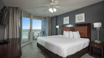 Une chambre d’hôtel avec un grand lit, un ventilateur de plafond, un bureau avec un téléphone, une chaise, un balcon avec vue et deux lampes fixées au mur.