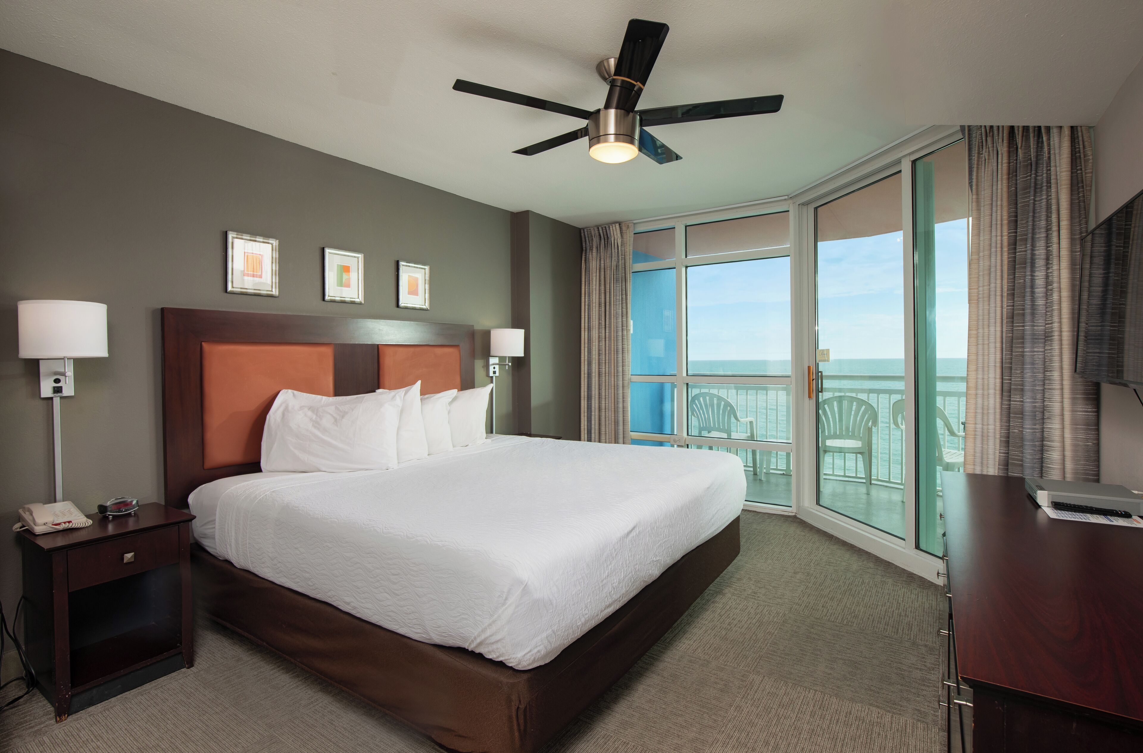 A hotel room with a large bed, a ceiling fan, a TV, and a balcony with a view.