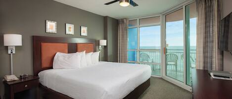 A hotel room with a large bed, a ceiling fan, a TV, and a balcony with a view.