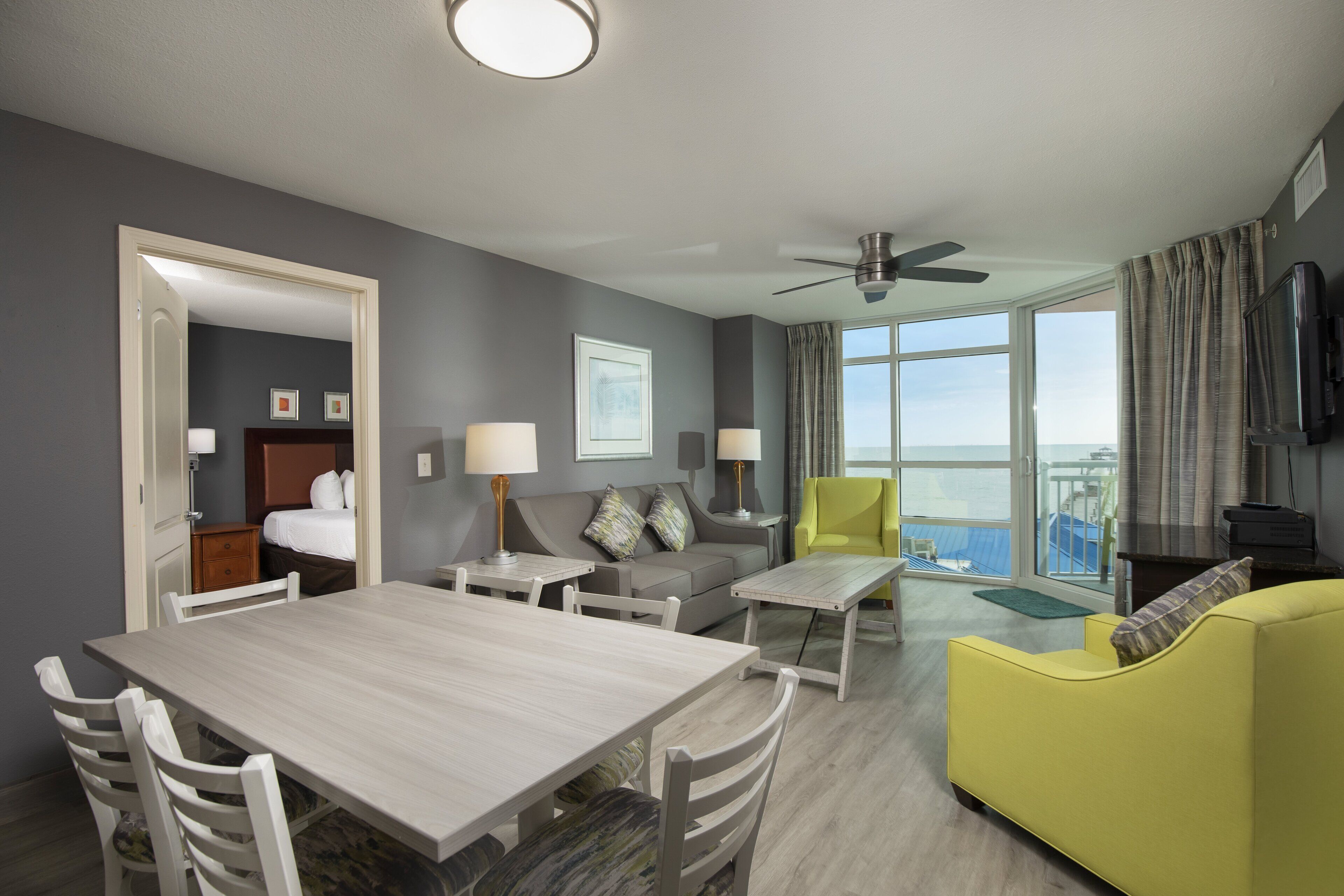 Habitación de hotel moderna con comedor, sofá, sillón amarillo y un gran ventanal con vistas.