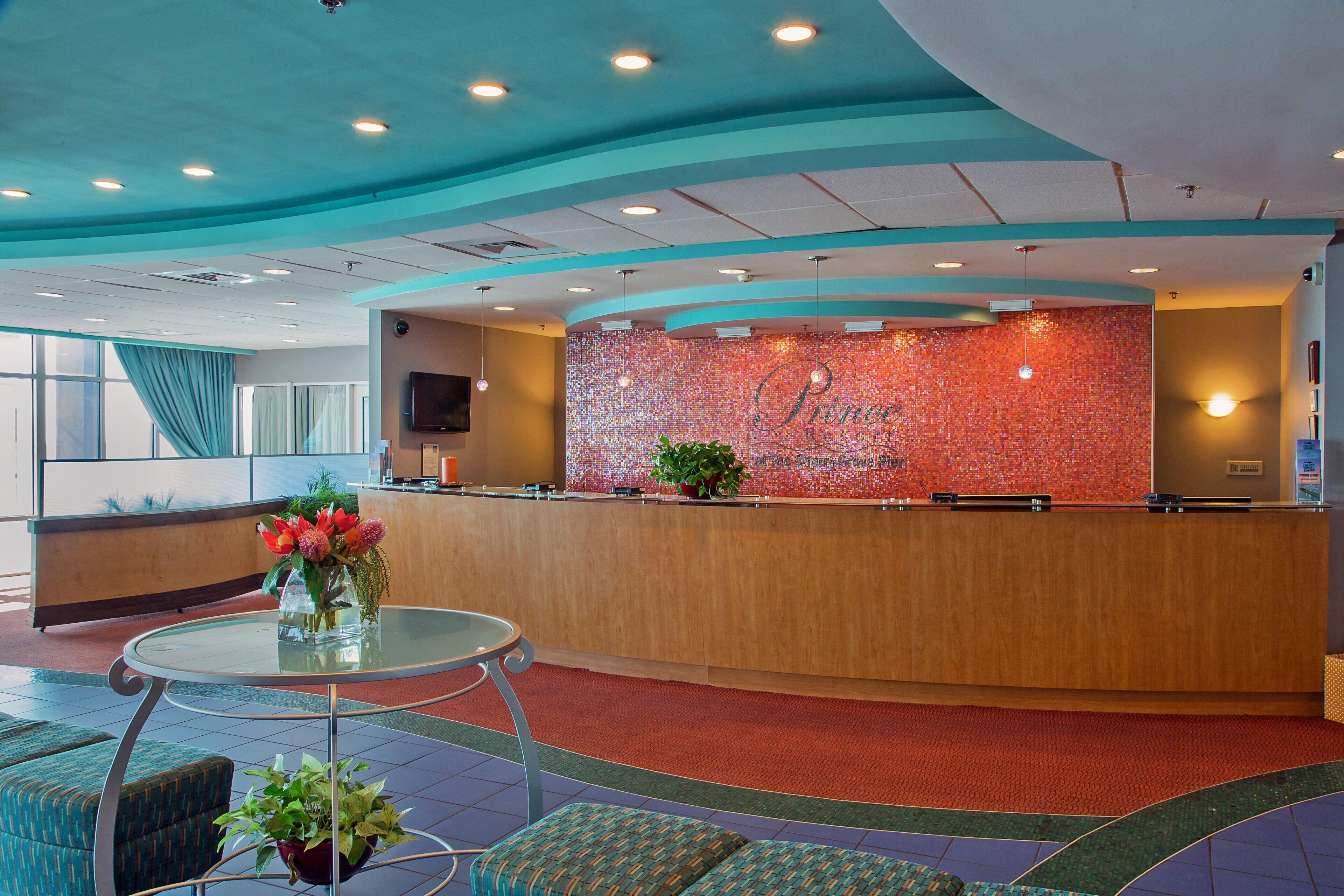 A hotel reception area with a curved reception desk, a television mounted on the wall, and a potted plant on the counter.