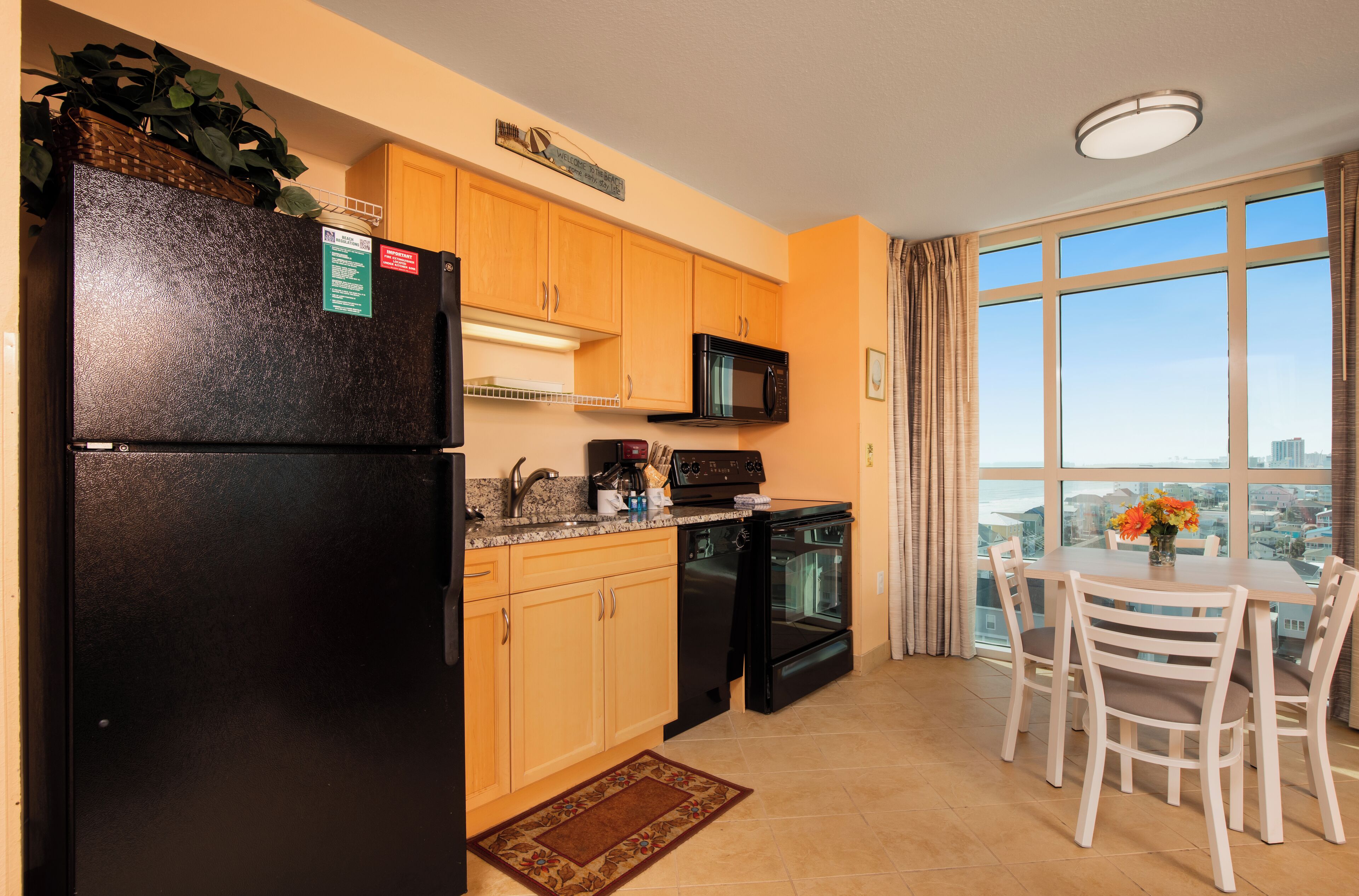 A kitchen with wooden cabinets, a black refrigerator, a microwave, an oven, and a dining table with chairs.