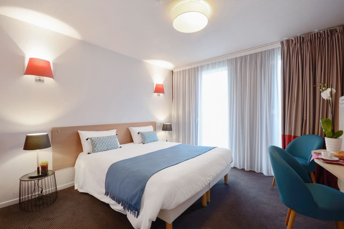 Une chambre d’hôtel avec un grand lit, deux lampes de chevet, un bureau avec une chaise et une fenêtre avec des rideaux.