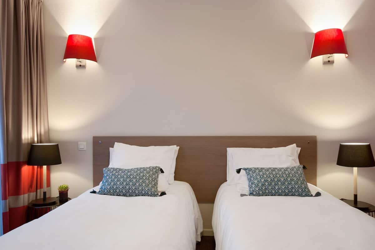 Une chambre d’hôtel avec deux lits, chacun doté d’un oreiller à motifs, d’une tête de lit en bois et de deux lampes fixées au mur.