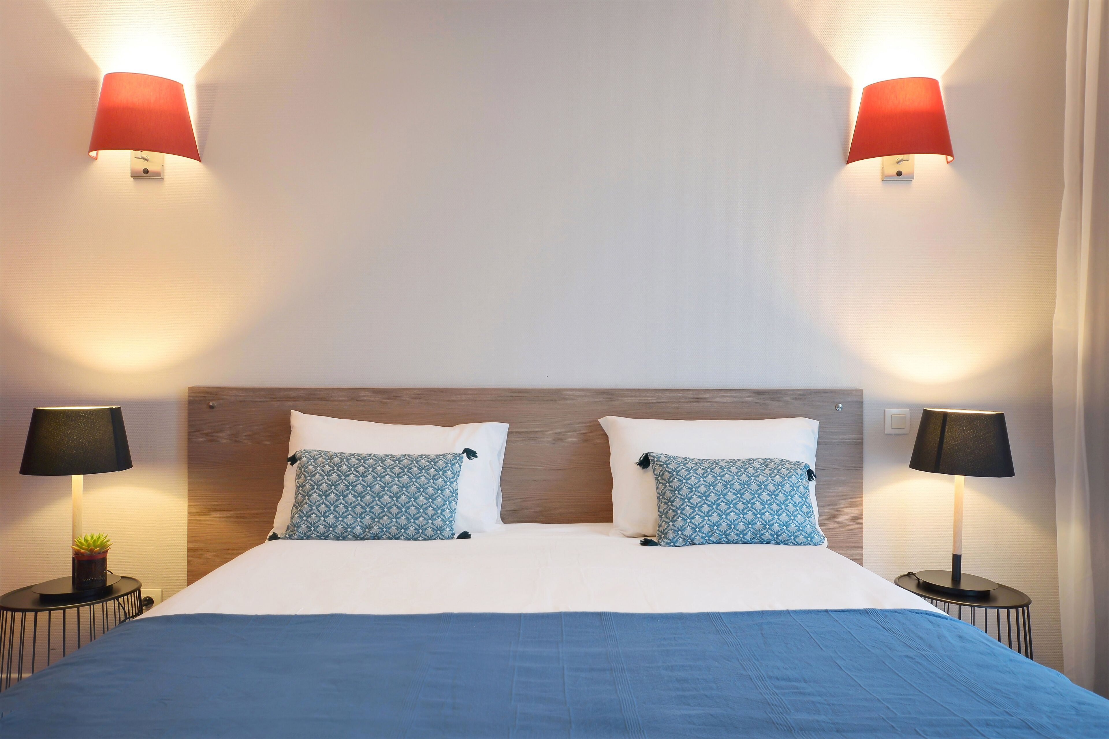 A hotel room with a bed, two bedside lamps, and a nightstand with a plant.