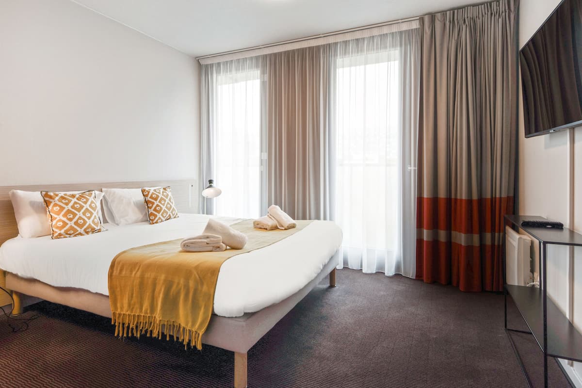 Une chambre d’hôtel avec un grand lit, une table de chevet, une télévision et une fenêtre avec des rideaux.