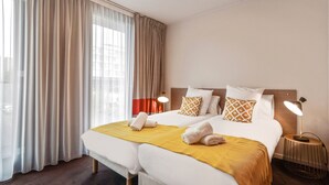 Een hotelkamer met een tweepersoonsbed, twee kussens, een bedlampje en een raam met gordijnen.