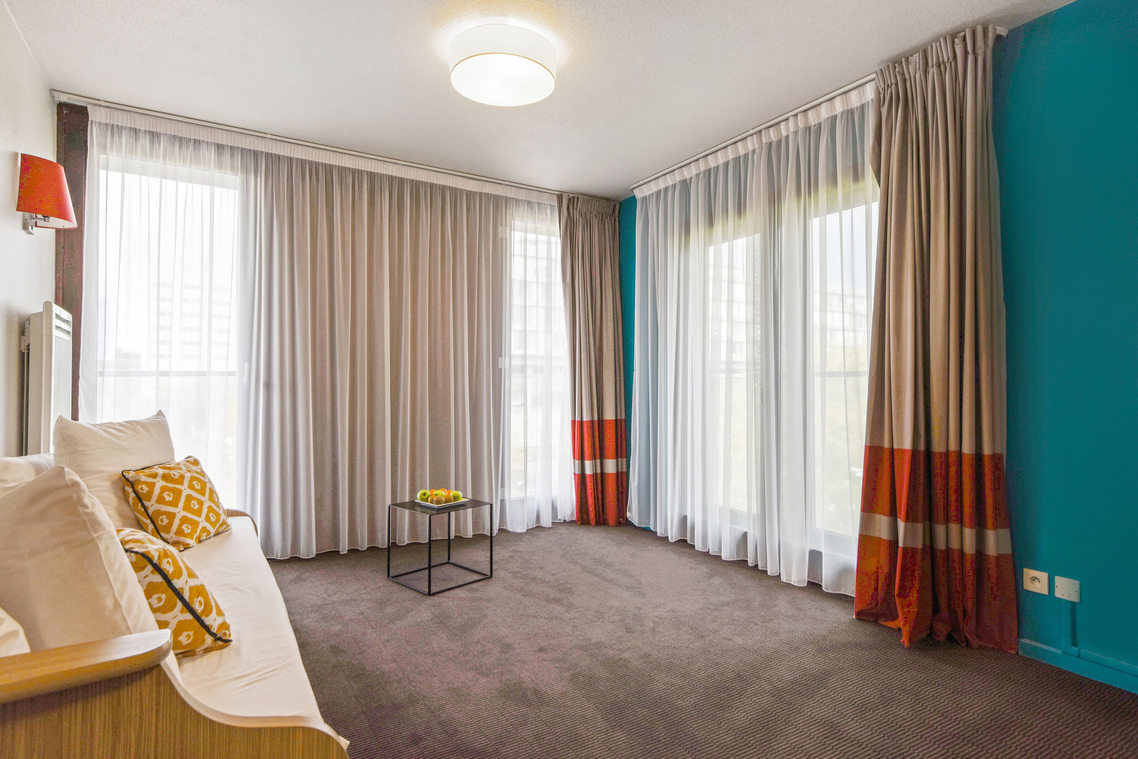 Een hotelkamer met een groot bed, een klein tafeltje met fruit en gordijnen voor de ramen.