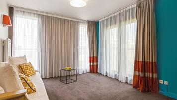 Een hotelkamer met een groot bed, een klein tafeltje met fruit en gordijnen voor de ramen.