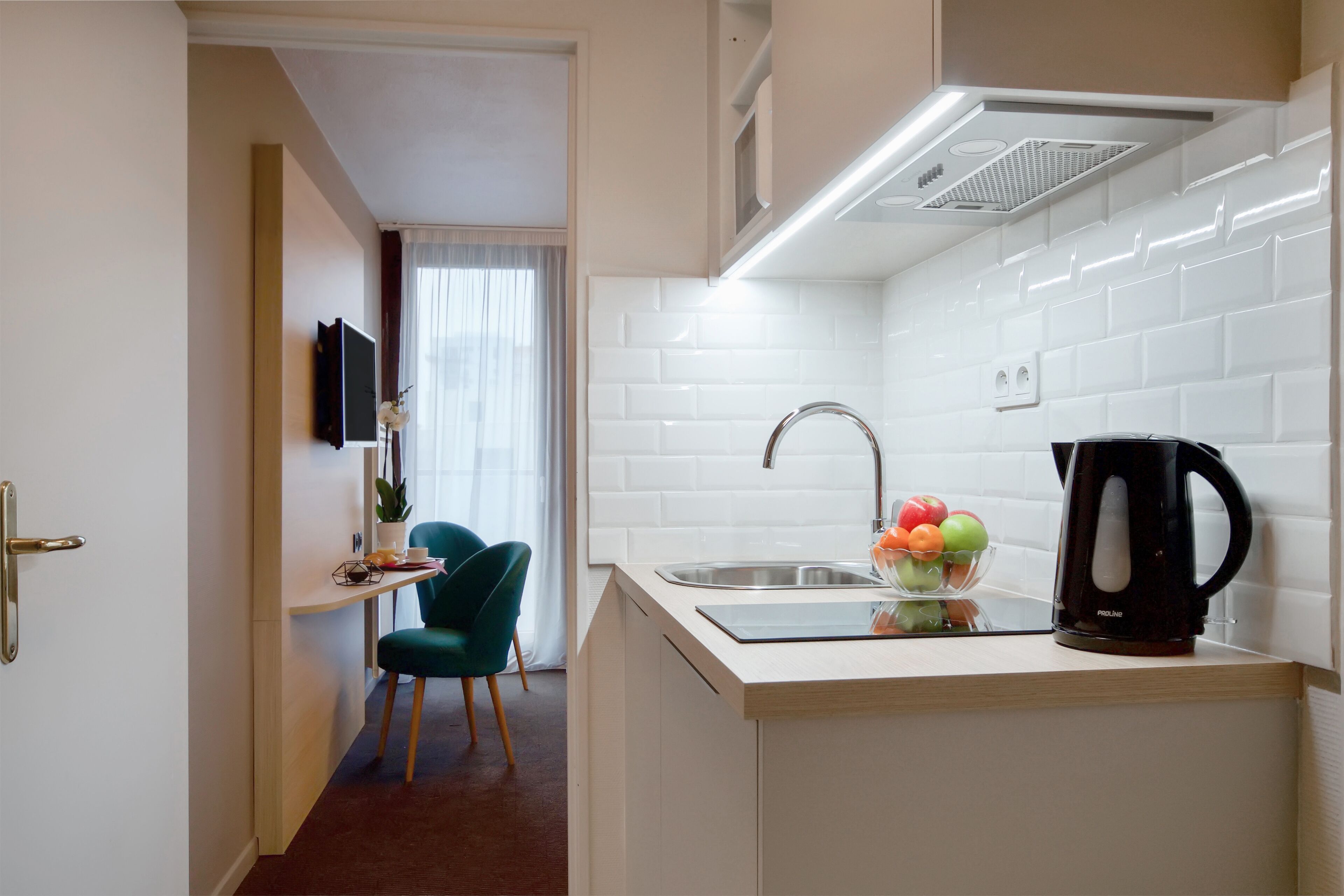 Une petite cuisine équipée d’un évier, d’une machine à café noire et d’un saladier rempli de fruits.