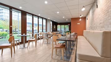 A spacious indoor area with tables and chairs, large windows, and a brick wall.
