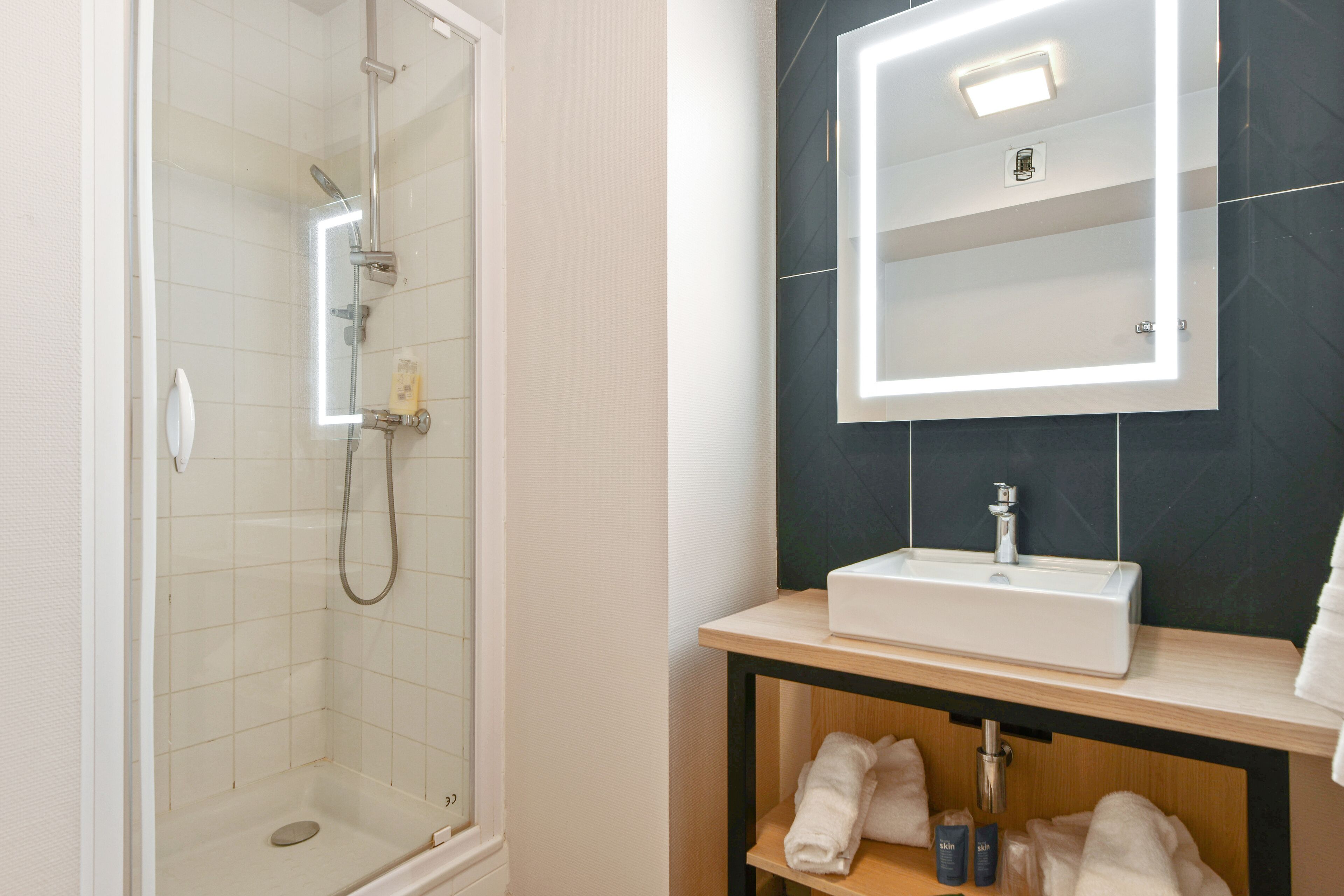 A bathroom with a glass-enclosed shower, a white sink, and a mirror with built-in lighting.