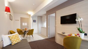 Een moderne hotelkamer met een bed, een bureau met een computer, een televisie en een zithoek met stoelen.