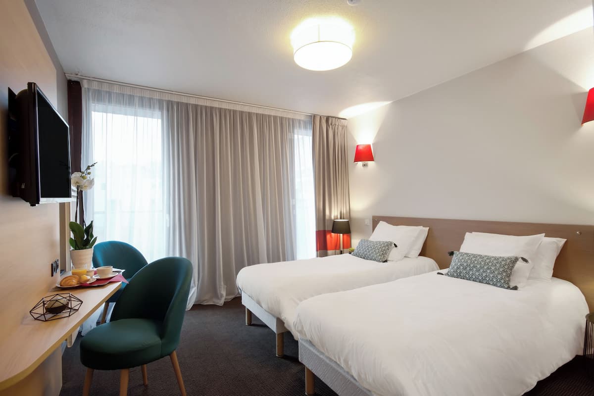Une chambre d’hôtel avec deux lits, un bureau avec une chaise, une télévision et une fenêtre avec des rideaux.