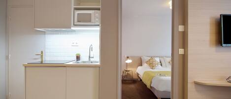 Habitación de hotel compacta con kitchenette, una cama con mesita de noche y un televisor montado en la pared.