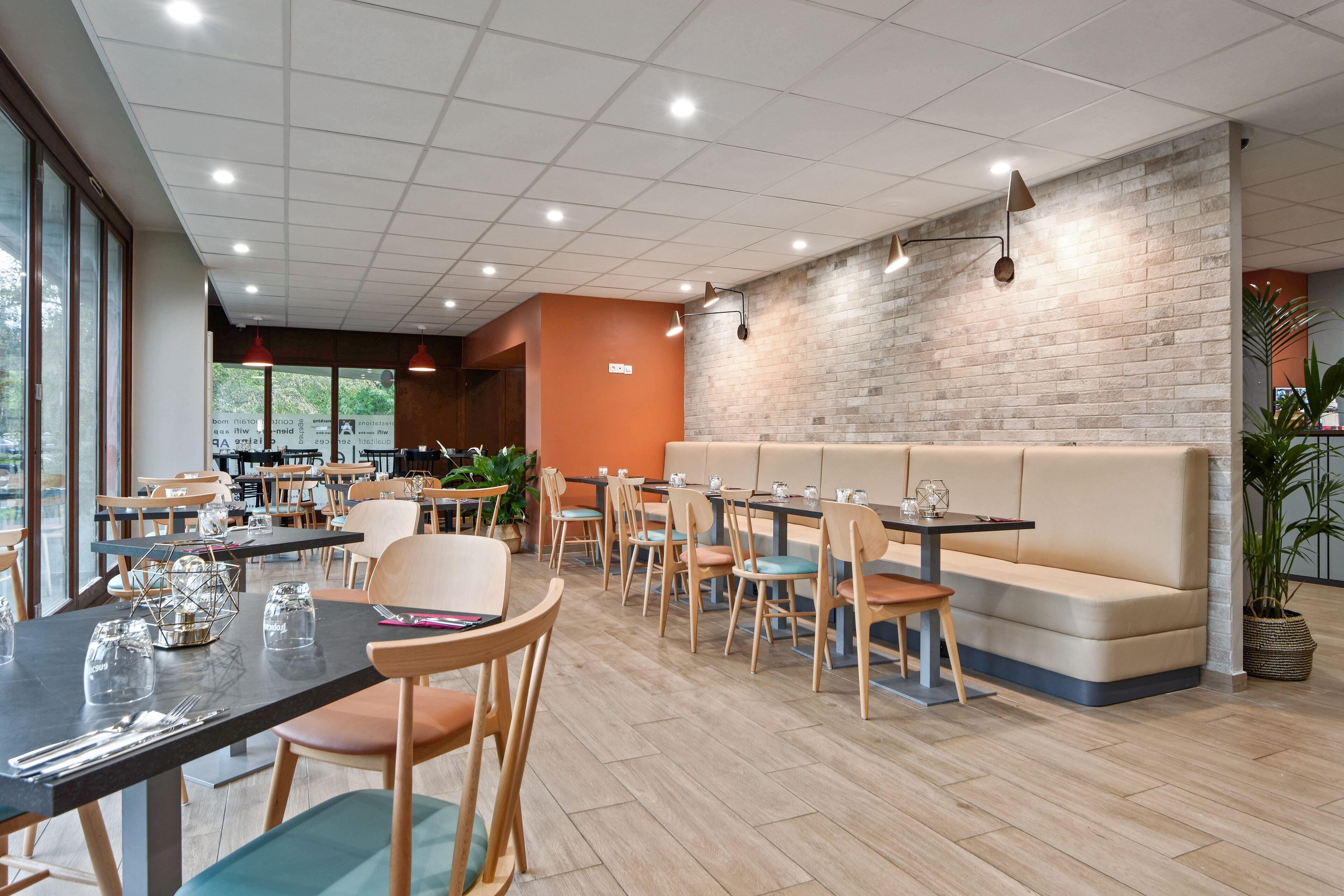 Ein modernes Restaurant-Interieur mit Holztischen und -stühlen, einer Ziegelwand als Gestaltungselement und einer Sitzgruppe mit gepolsterten Bänken.
