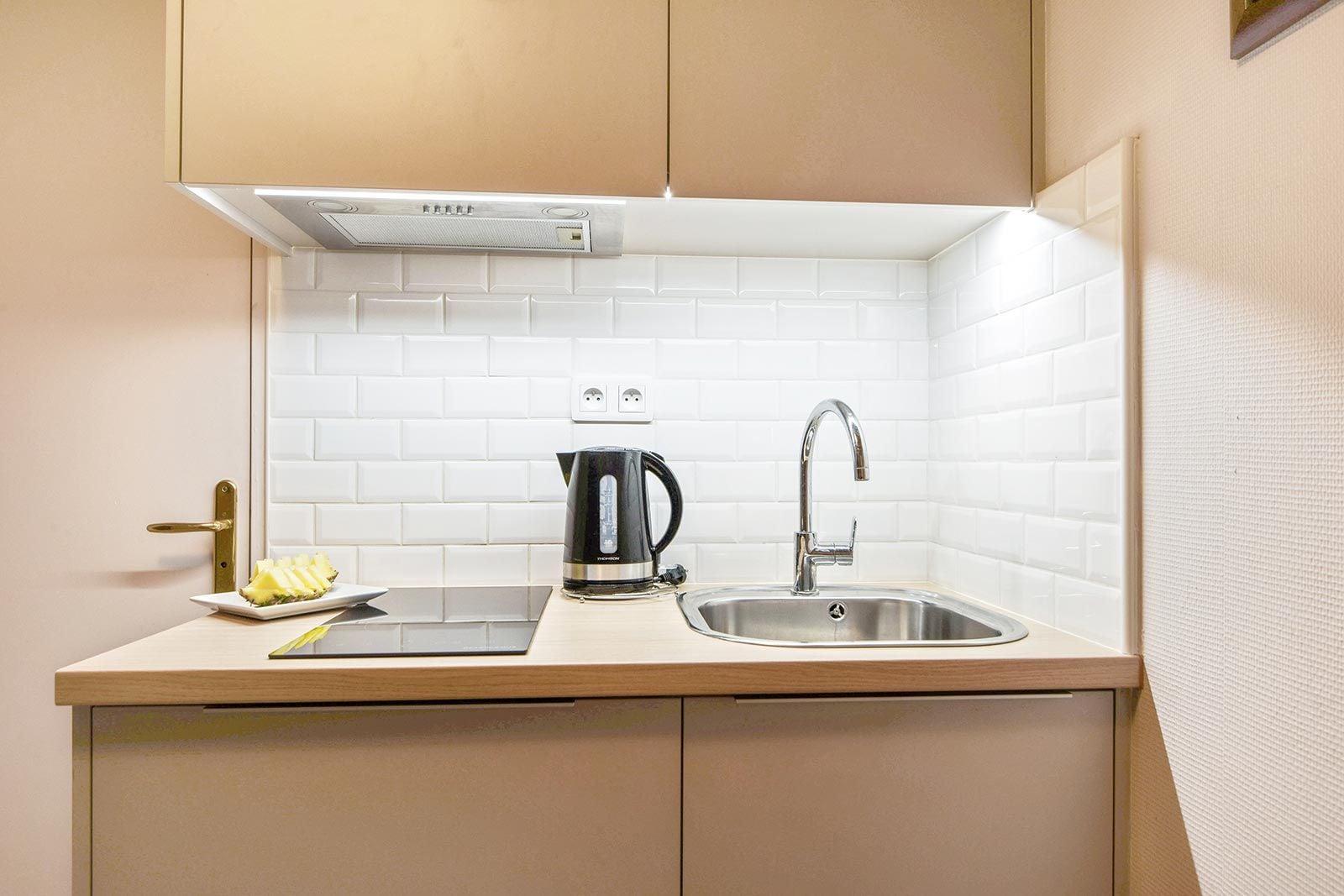 Een kleine keuken met een spoelbak, een waterkoker en een bord eten.