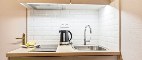 Una cocina compacta con un lavamanos, una cafetera y un plato pequeño con comida.