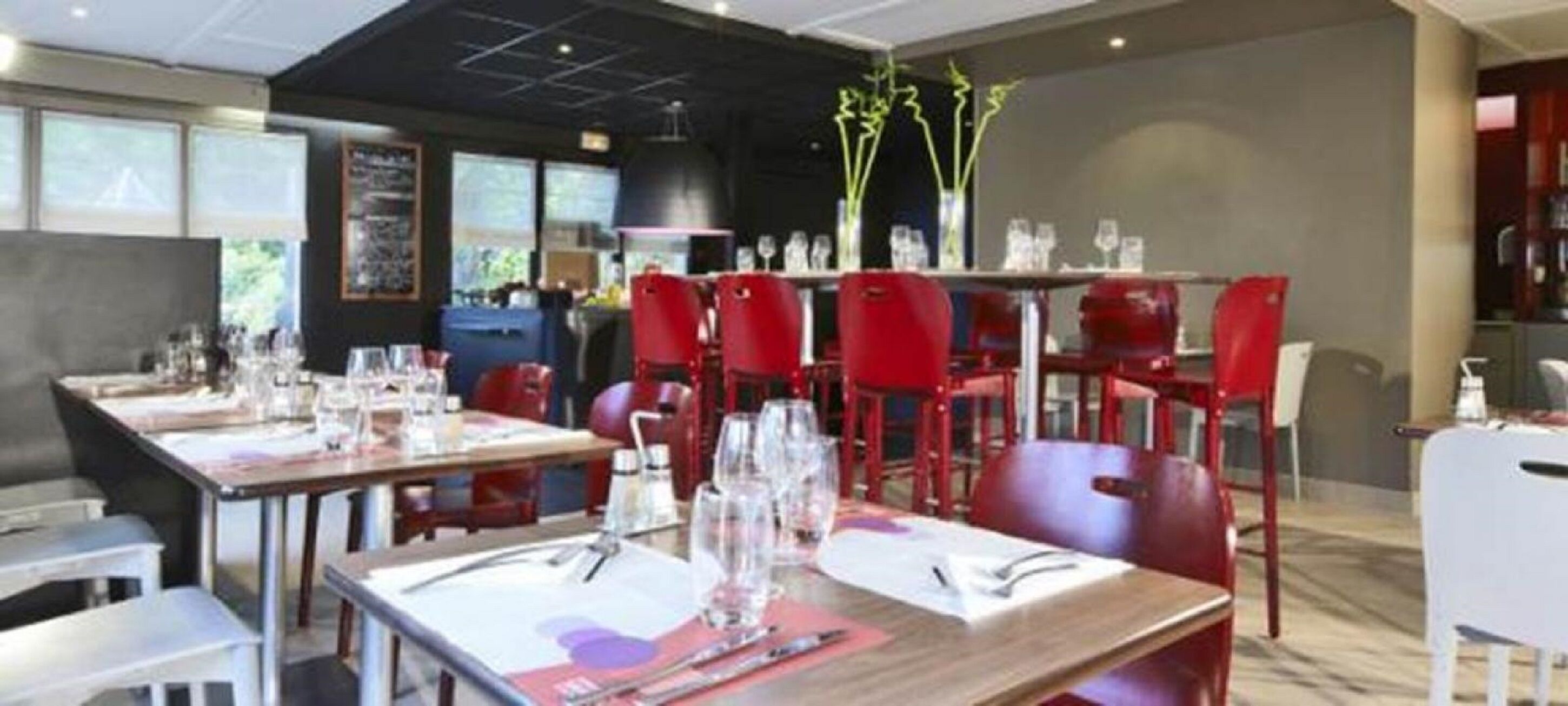 Un interior de restaurante con mesas dispuestas para comer, sillas rojas y una zona de bar al fondo.